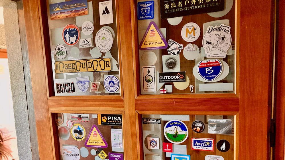 A bunch of stickers are hanging on a window pane, including one that says Outdoors on it.