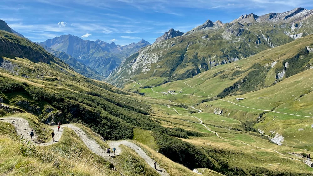 A couple are hiking up a mountain with the top in the distance.