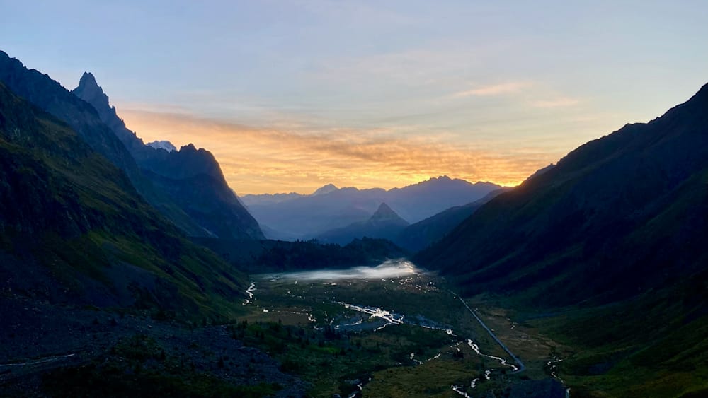 A valley with a sunset behind it and mountains in the background.