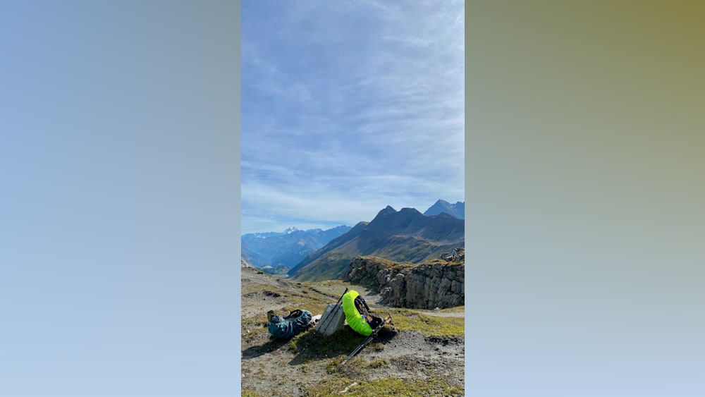 A man is setting up camp on a mountain with his yellow and black backpack.