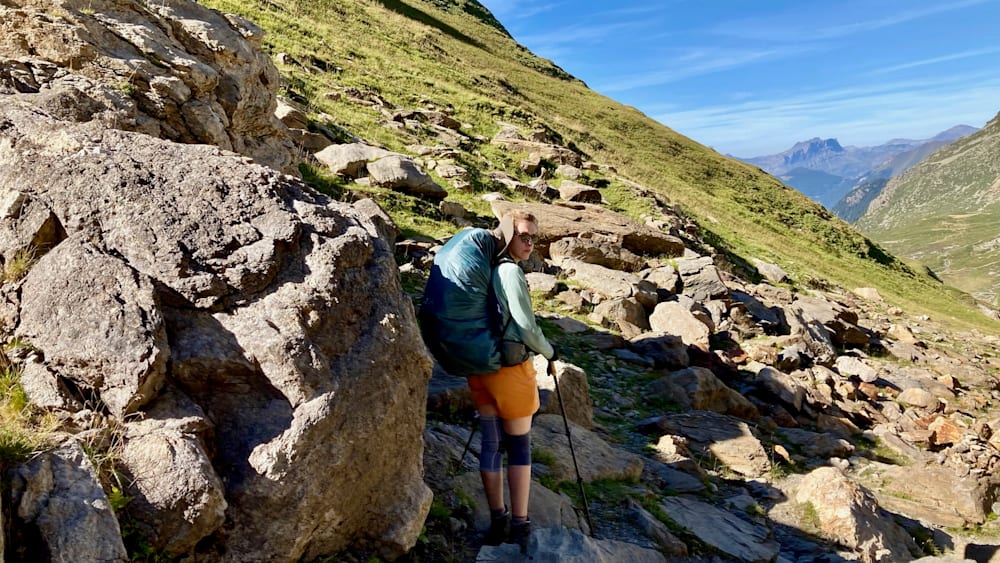 A woman with a green and orange shirt standing on a mountain with a backpack.