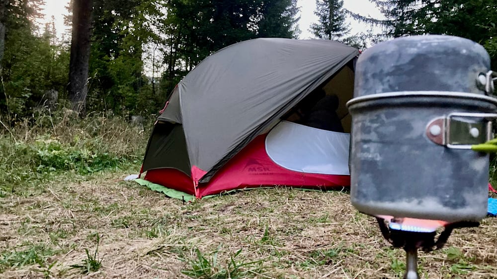 A MSR tent is set up on a grassy area with a black and white sleeping bag inside.