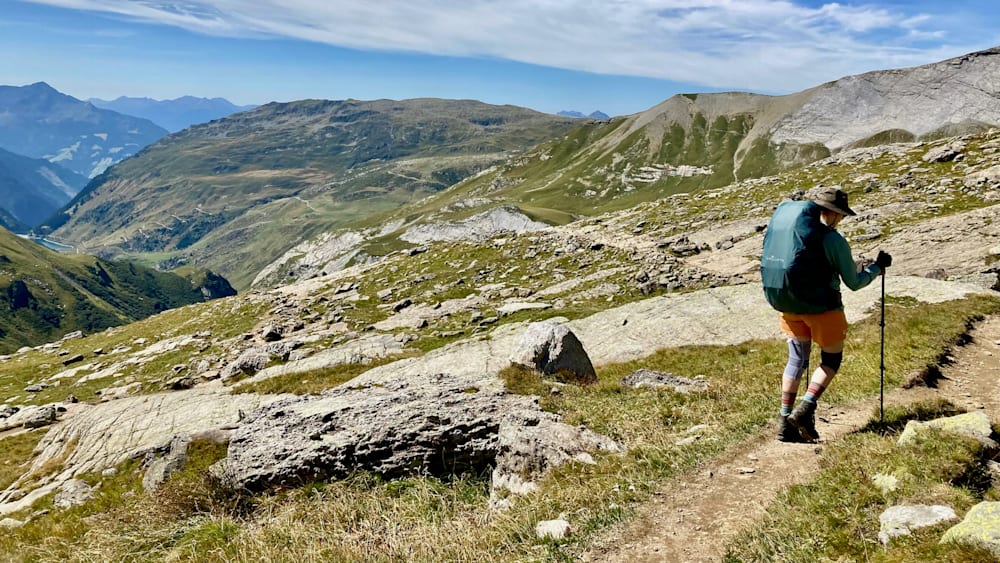 A person standing on a mountain with a blue shirt and blue backpack.