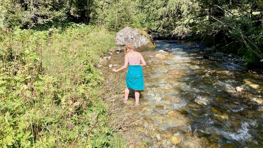 A woman in a blue skirt is walking through water in a stream.