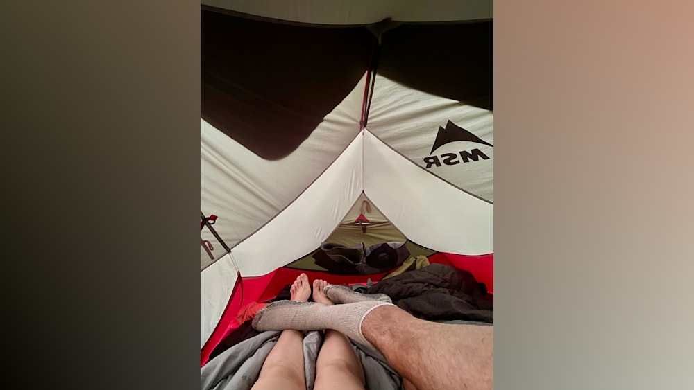 Two people with socks on their feet in a tent with the words MSR on it.