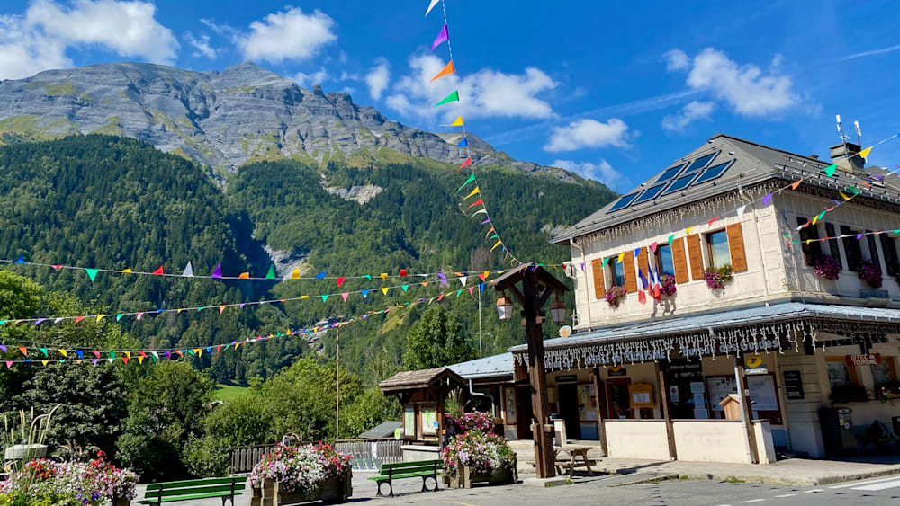 colorful flags strung between buildings on a street near a mountain.
