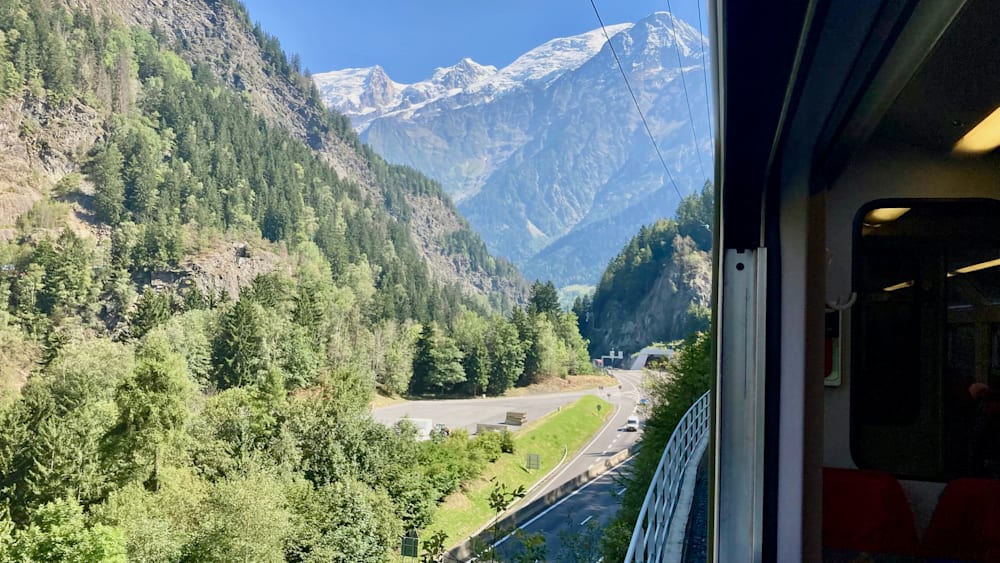 A road goes through a forest and over a bridge before continuing on to the mountains.