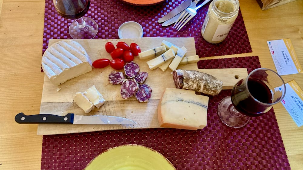 A wooden cutting board with various foods on it, including some type of meat and cheese, and a bottle of wine.