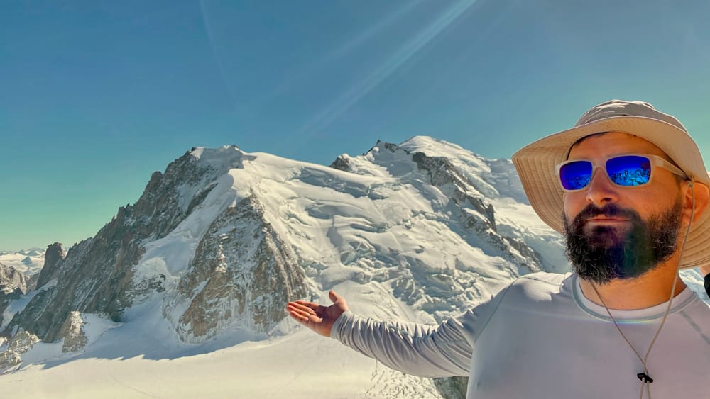 A person in a white shirt points toward a mountain.