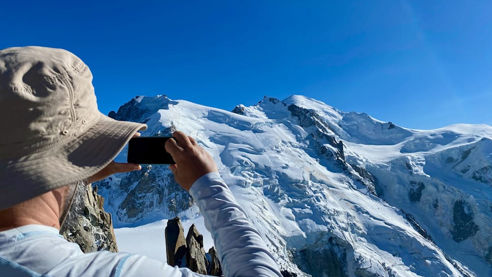 A man taking a photo of a mountain with his phone.