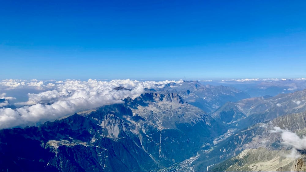 An aerial view of a mountain range with clouds and a town in the valley below.