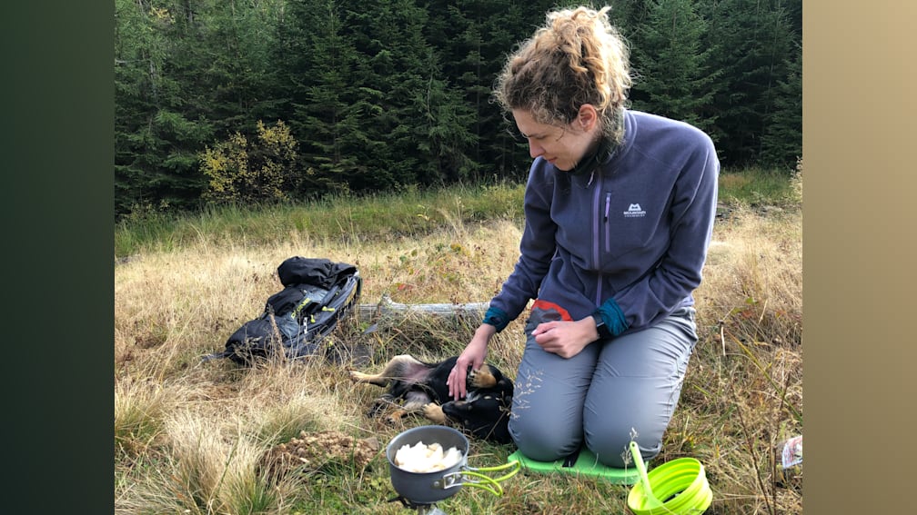 A woman kneeling down next to a dog which is licking her hand.