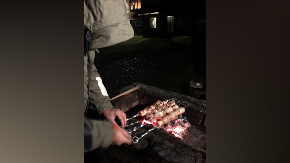 A person is cooking some meat on a BBQ at night.