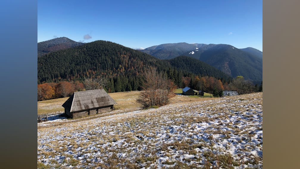 A snowy field with a cabin in the woods and a field of grass.