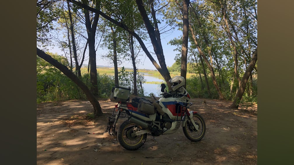A person is taking a picture of a motorcycle parked next to a lake.