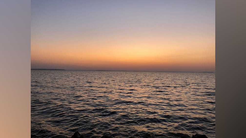 A sunset over a large body of water with the water appearing very dark.