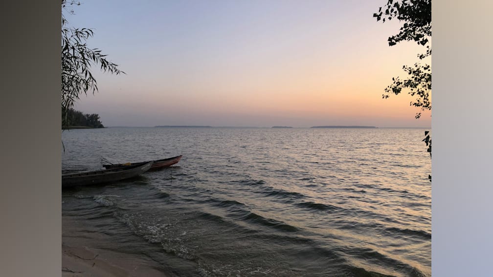 A boat is floating on a body of water with the sun setting in the background.