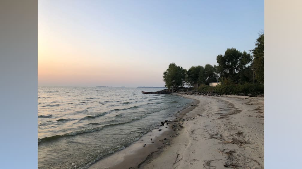 A beach at sunset with the water and sand and a boat in the water.