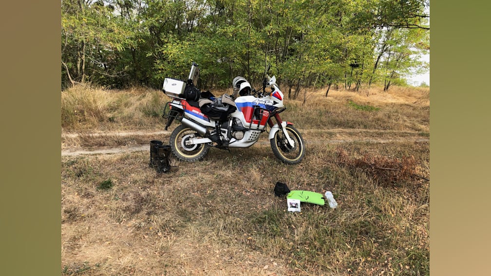 A person is leaning on a motorcycle in a field.