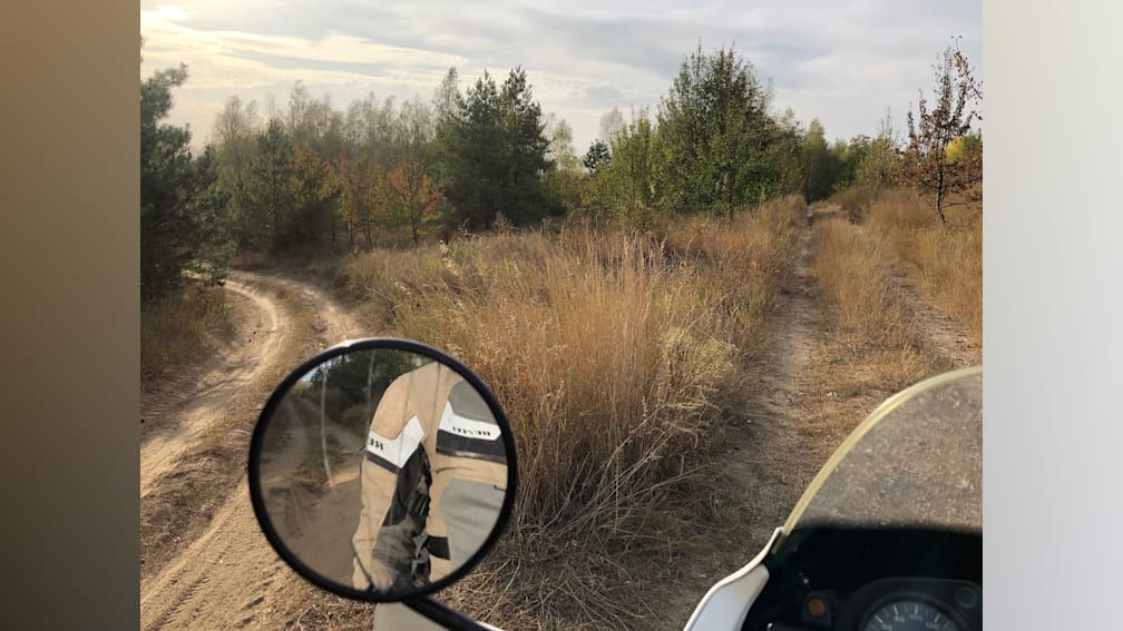 A side view mirror of a motorcycle showing a large, grassy field.