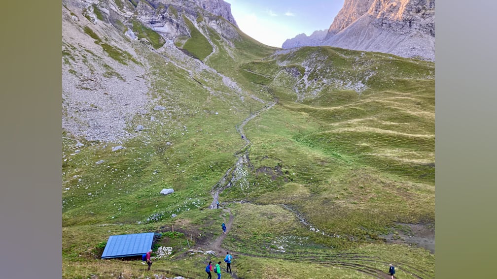 Several people walking up a hill with a blue roof in the background.