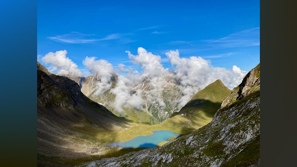 A mountain lake with a blue water and clouds in the background.
