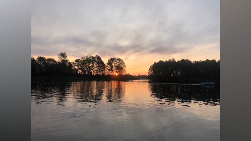 The sun is setting over a lake, creating a beautiful reflection on the water.
