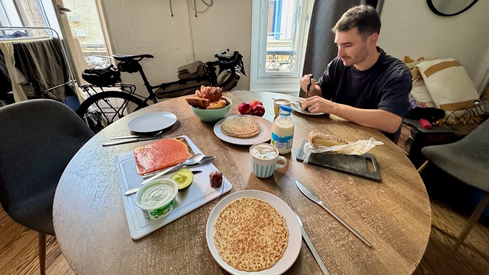 A man sits at a table eating breakfast with a cup of coffee.