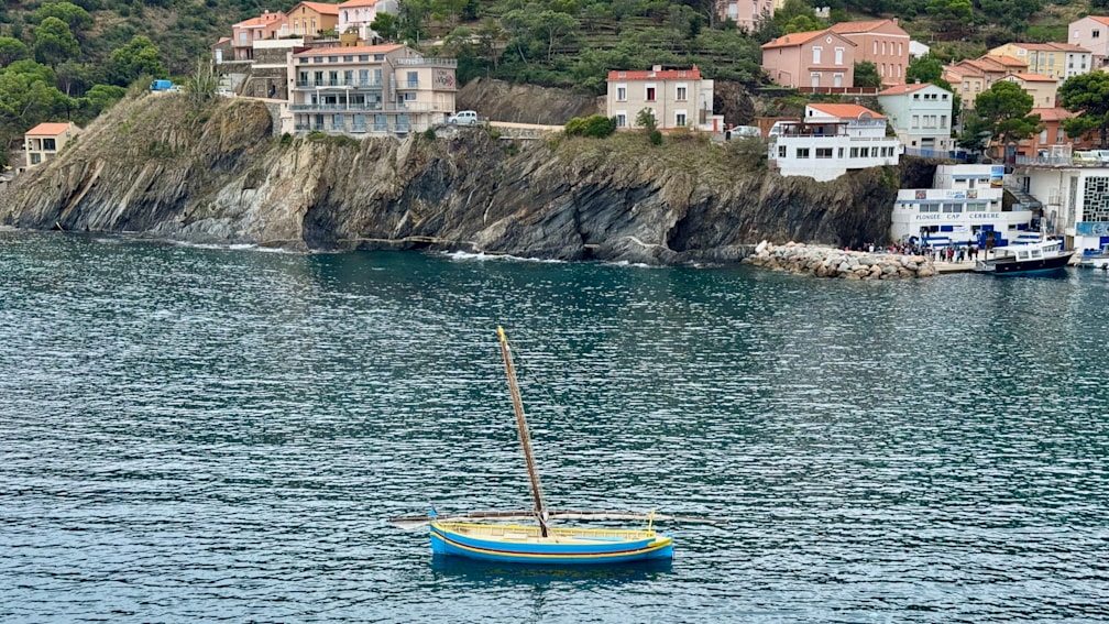 A small sailboat on a lake near shore with a cliff in the background.