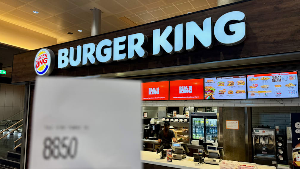 A burger king store with people inside and a sign out front advertising their deals.