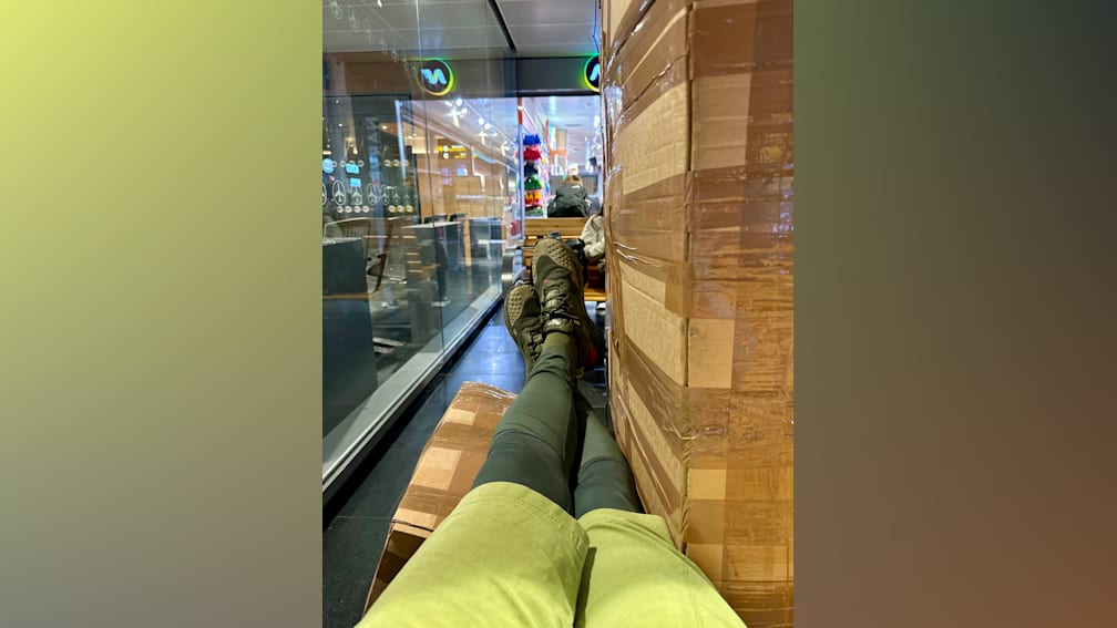 A person in a green shirt is sitting next to a wall of cardboard boxes.