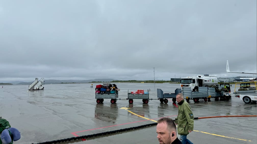 People are loading luggage onto carts in a parking lot on an overcast day.