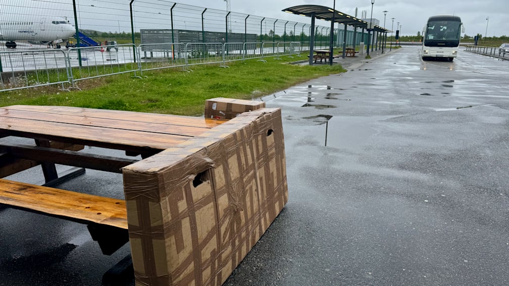 A large wooden bench is strapped to a cardboard box on a wet sidewalk.