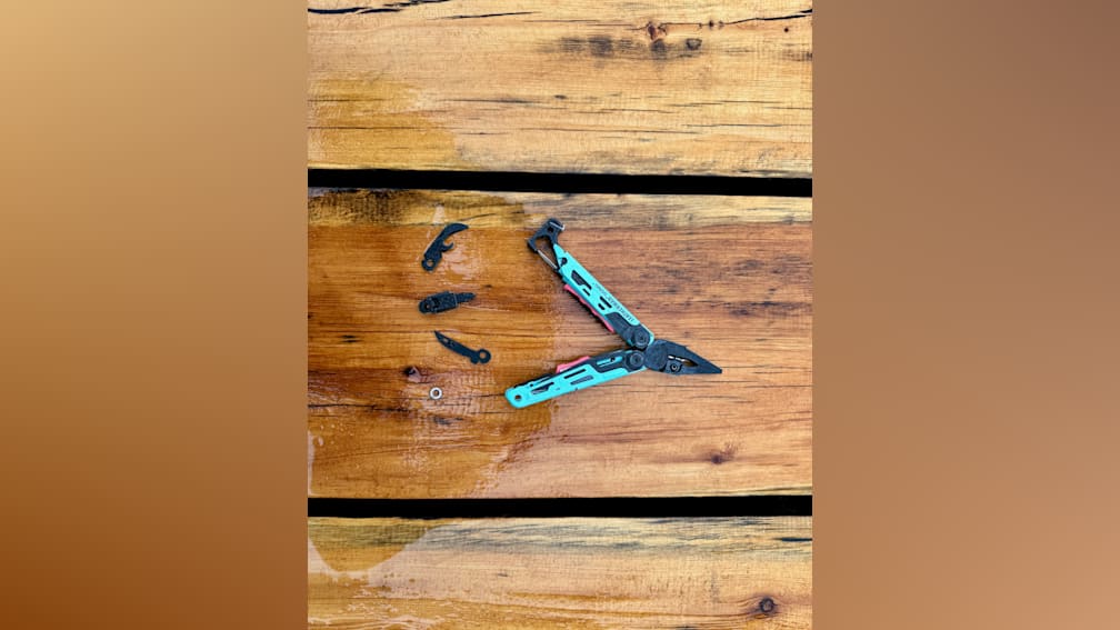 A multitool with a blue handle is laying on a wet wooden surface.