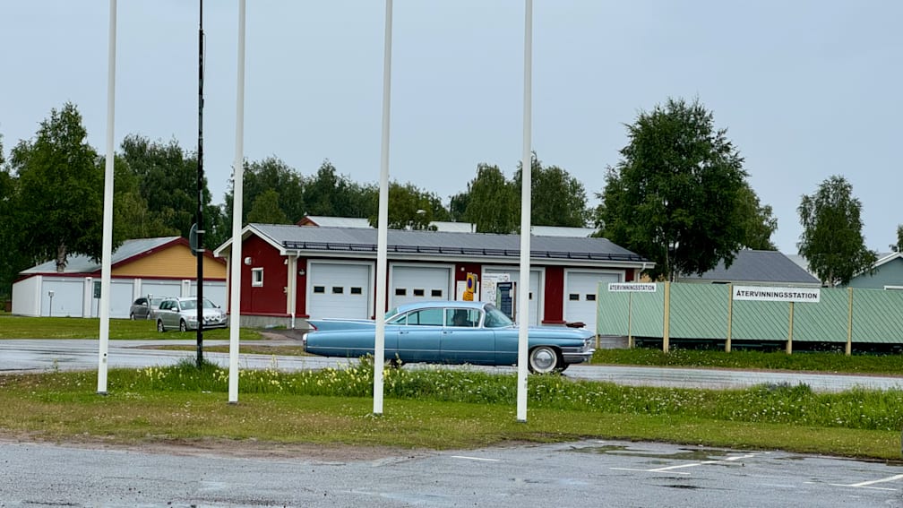 A blue car is parked in front of a red garage.