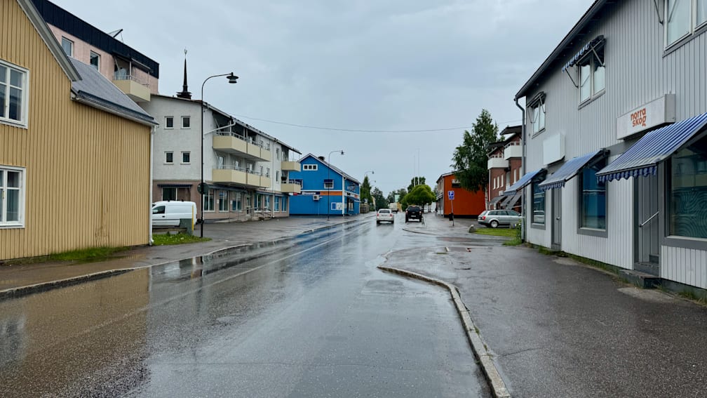 A wet street in the rain with a blue house at the end of the road.