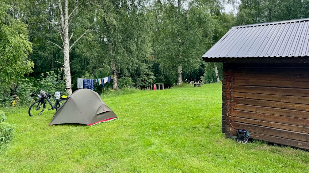 A tent is pitched in a grassy field next to a building.
