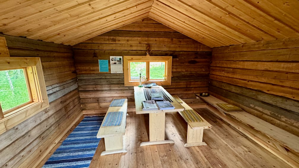 A rustic cabin with a table and bench in the center of the room.