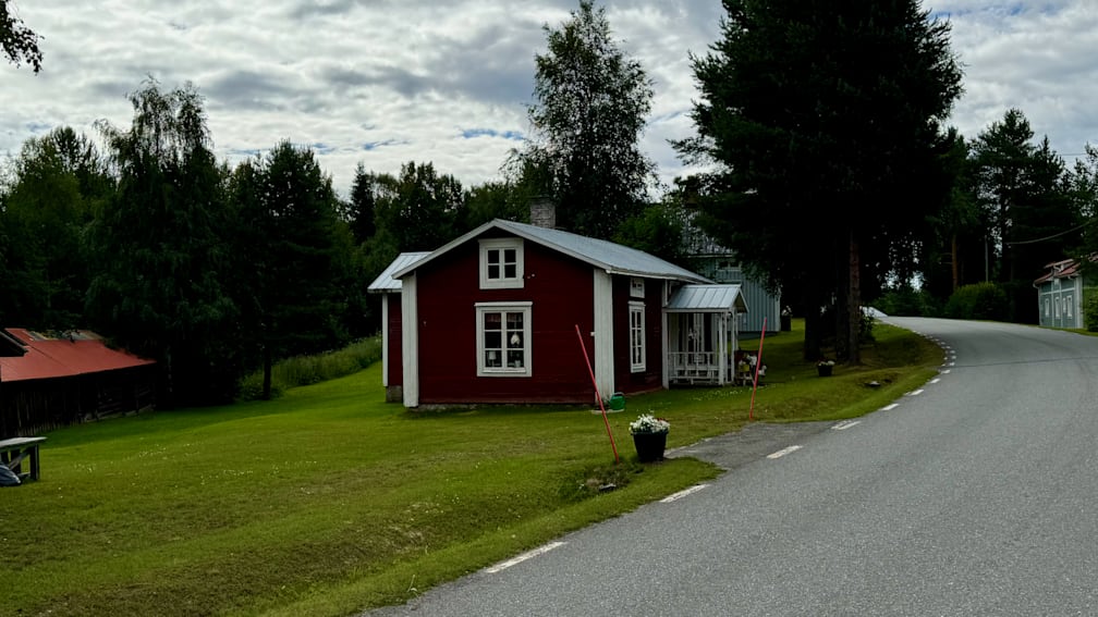 A red house on a green lawn with a porch and a pot of flowers in front.
