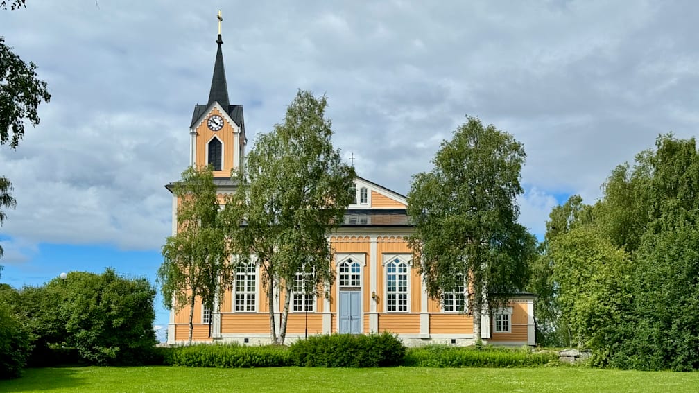 A church with orange and yellow steeples and a green grassy field in the background.