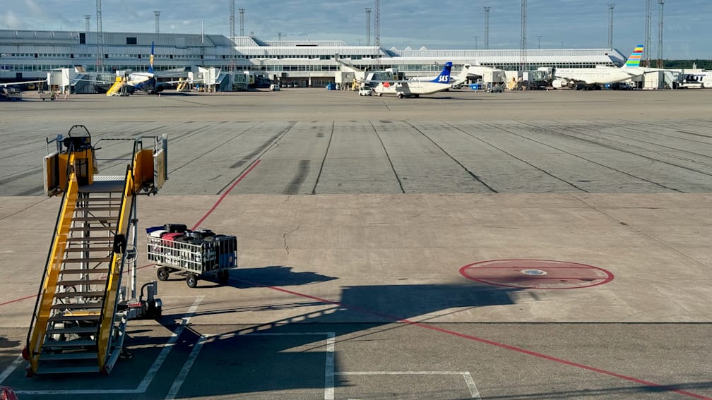 An airport tarmac with a cart in front of a plane with suitcases on it.