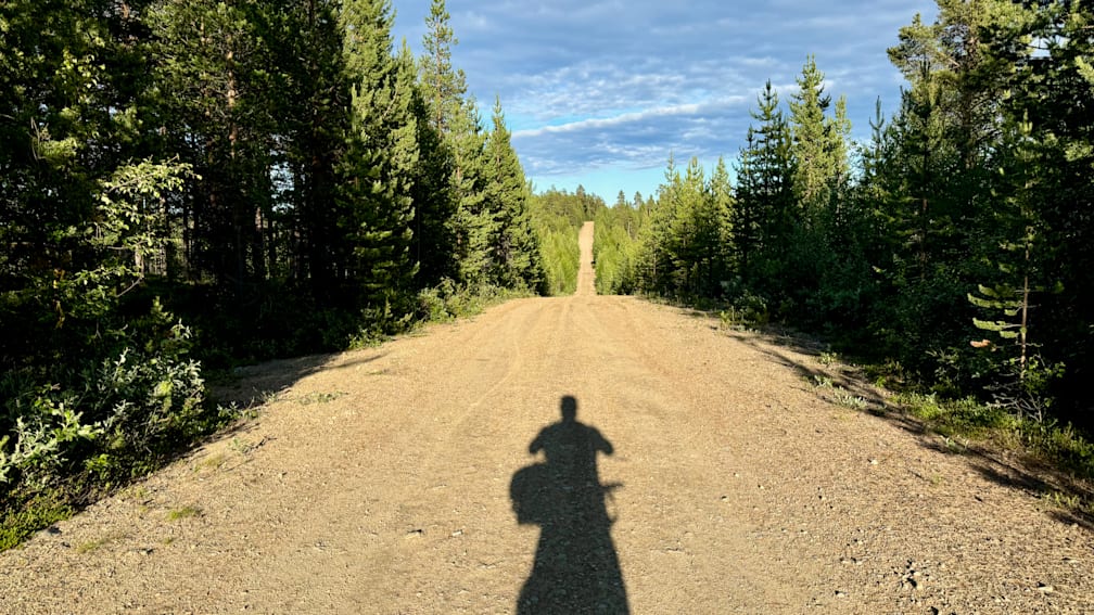 A motorcycle rider's shadow is cast on the road as he rides down the road.