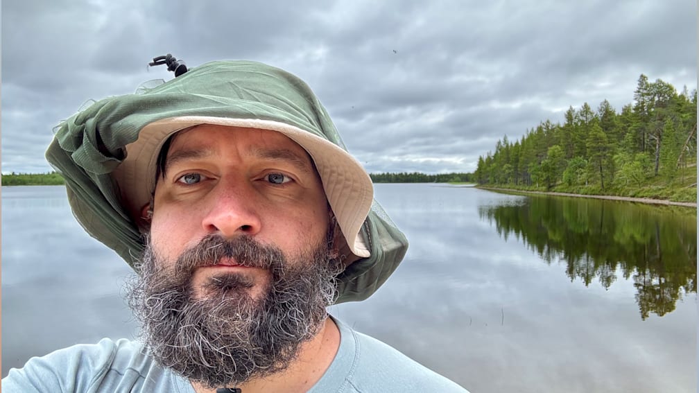 A man wearing a hat looks out at a lake.