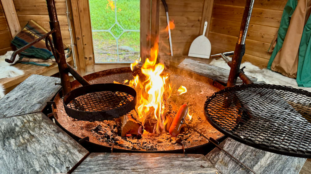 A fire is burning in a grill and cooking some hot dogs while a spatula is nearby to flip them.