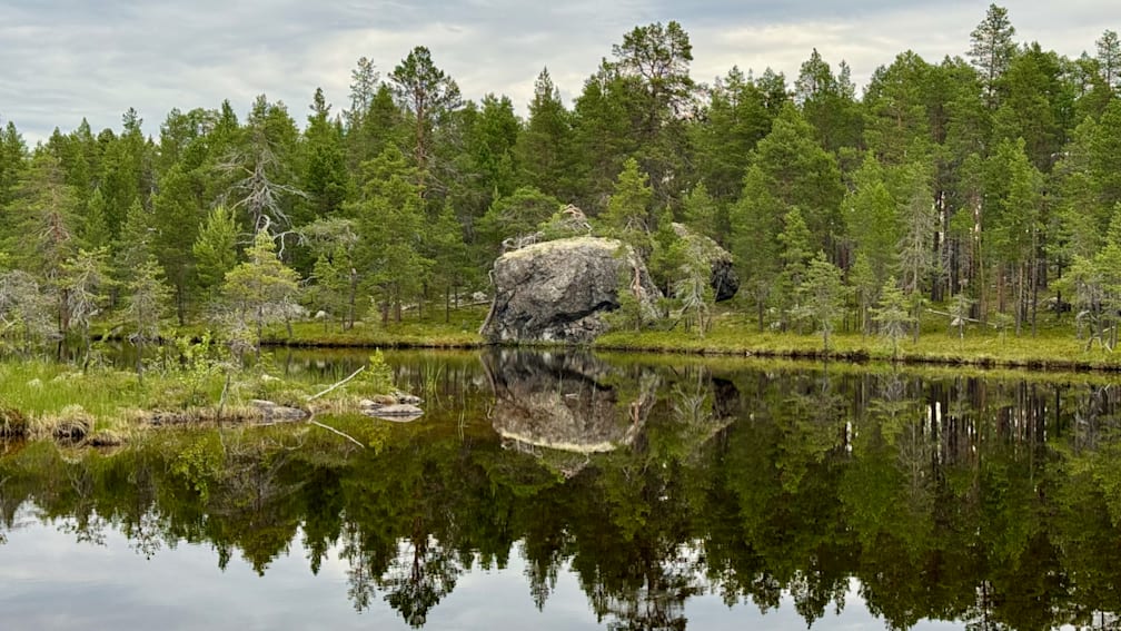 A large rock is in the water and creating a reflection.