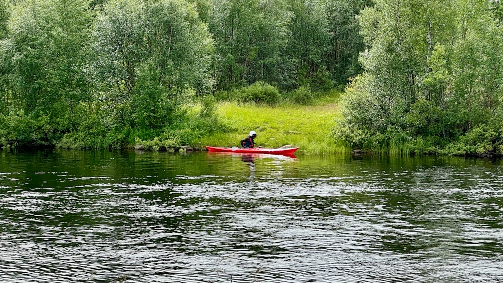 A man in a red kayak on a body of water with trees in the background.