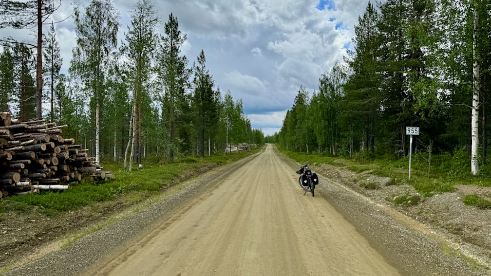 A dirt road is ahead and a person is on the back of a bike.