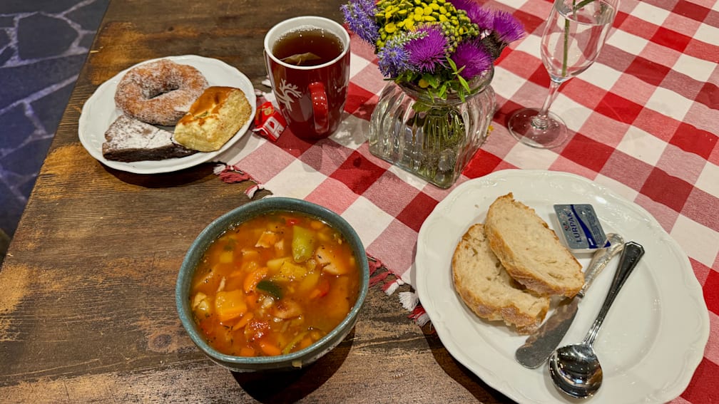 A table with a plate of food and a glass of tea with a vase of flowers in between.
