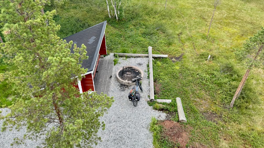 A bike is parked on gravel next to a red shed.