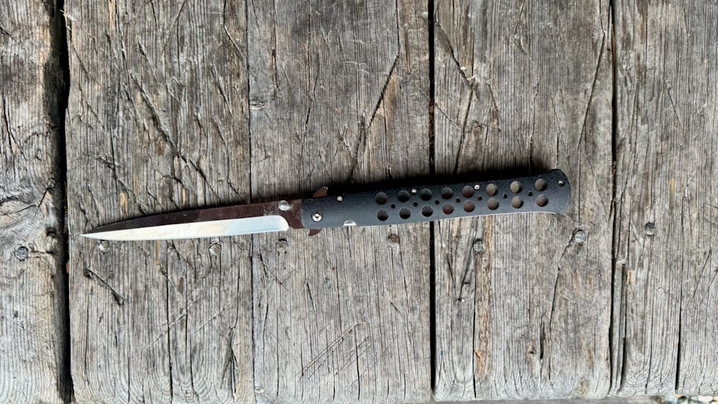 A small, black, blade edge knife lies on a wooden surface.